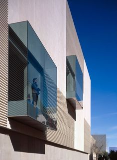 a man walking down the street in front of a building with glass balconies