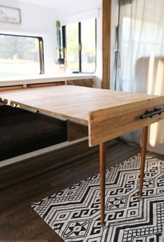 a wooden table sitting in the middle of a living room next to a white rug