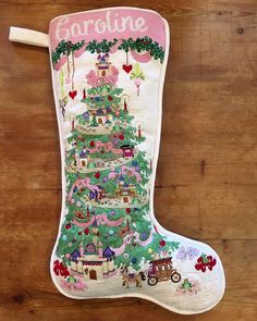 a stocking with a christmas tree on it is hanging from a wooden floor and has the word caroline written in pink