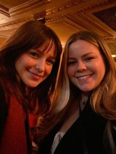 two women standing next to each other in a room with lights on and one woman is smiling at the camera