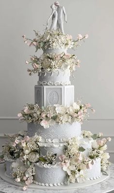 a three tiered wedding cake with flowers on the top and two figurines atop it