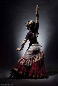 a woman is dancing with her arms in the air while wearing a red and gold skirt