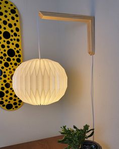 a white lamp hanging from the ceiling next to a potted plant on a table