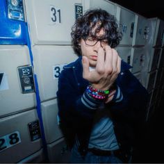 a young man wearing glasses and holding his hand up to his face in front of lockers