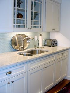 a kitchen with white cabinets and marble counter tops, along with a stainless steel sink