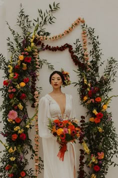 a woman standing in front of a wall with flowers and greenery around her head