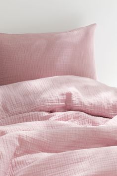 a bed with pink sheets and pillows on top of it, next to a white wall