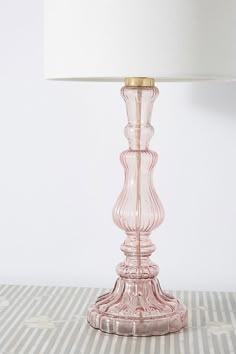 a pink glass table lamp with a white shade on the top and bottom part of it