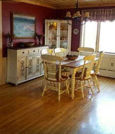 a dining room table with yellow chairs and a china cabinet in the corner, next to a window