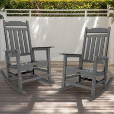 two gray rocking chairs sitting on top of a wooden deck next to a white fence