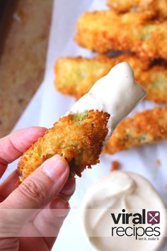 a person holding up a piece of food in front of some dipping sauce on the side