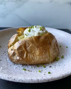 a baked potato with sour cream and chives on it sits on a white plate