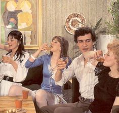 three women and two men sitting on a couch with drinks in their hands, drinking