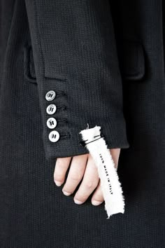 a person in a black suit with buttons on their lapel and one hand holding a white piece of paper