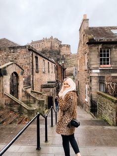 a woman in leopard print coat and black pants standing on steps next to stone buildings