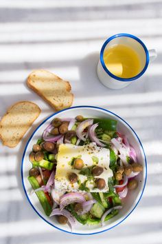 a bowl of food with bread and olives next to it on a white surface