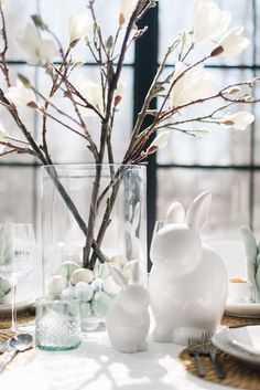 an easter table setting with white and green eggs, bunny figurines and branches