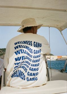 a man sitting on the back of a boat wearing a t - shirt that says wellness gang