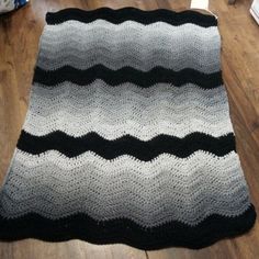 a black and white crocheted blanket sitting on top of a hard wood floor