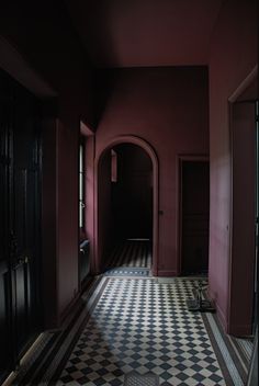 an empty hallway with black and white checkered flooring, red walls and doors