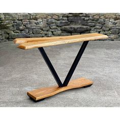 a wooden bench sitting on top of a cement floor next to a stone wall with black metal legs