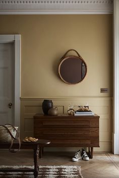 a living room with a wooden dresser and round mirror on the wall above it's door