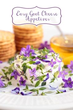 a plate topped with cheese covered in purple flowers next to crackers and olive oil