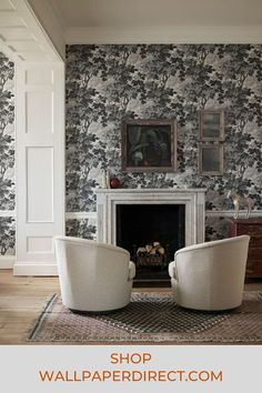 two white chairs sitting in front of a fireplace with a painting on the wall behind them