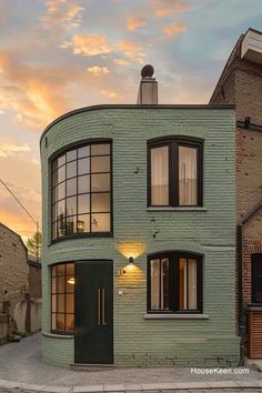 a green building with lots of windows next to a brick wall and street in front of it