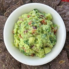 a white bowl filled with guacamole surrounded by tortilla chips