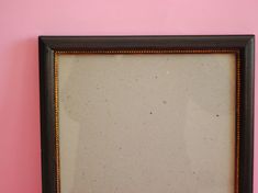 an old black framed mirror against a pink wall