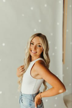 a woman standing in front of a white wall with her hands on her hips and looking at the camera