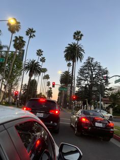 two cars are stopped at an intersection with palm trees in the background and traffic lights on both sides