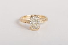 a yellow gold engagement ring with a cushion cut diamond in the center, on a white background