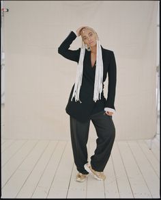 a woman in a black suit and white scarf posing for the camera with her hands on her head