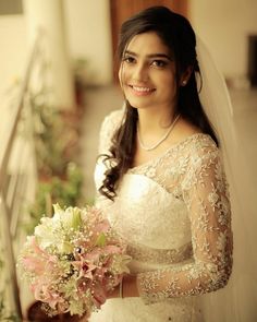 a woman in a wedding dress holding a bouquet and smiling at the camera while standing on a balcony