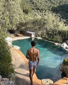 a shirtless man walking towards a swimming pool in the middle of a wooded area