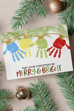 a christmas card with handprints on it next to pine branches and ornaments in the background