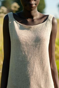 a woman standing in the grass wearing a white top with holes on it's chest