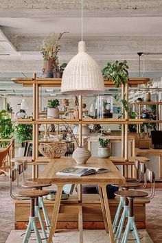 a wooden table surrounded by chairs and potted plants in a room with exposed ceilings