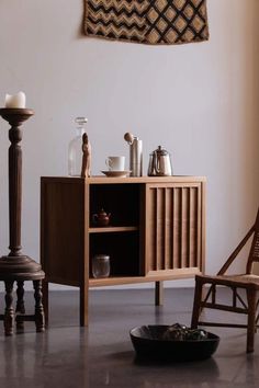 a wooden cabinet sitting next to a chair and table with dishes on top of it