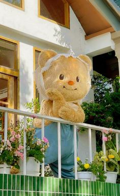 a large teddy bear sitting on top of a balcony next to potted plants and flowers