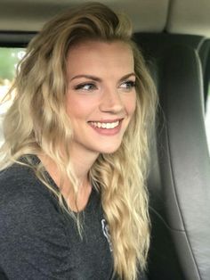 a woman sitting in the back seat of a car with blonde hair and blue eyes