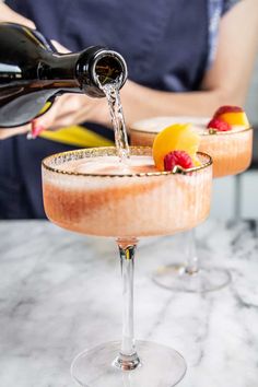 a person pouring champagne into a glass filled with fruit and ice on top of a marble table