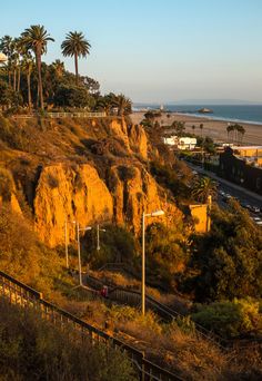 the sun is shining on some hills by the beach and ocean with palm trees in the foreground