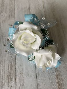 a white rose and blue ribbon corsage on a wooden surface with pearls, beads and ribbons