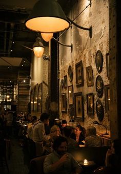 people sitting at tables in a restaurant with pictures on the wall behind them and lights hanging from the ceiling