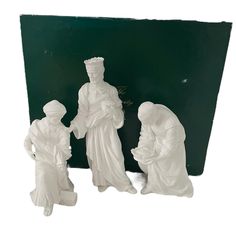 three white figurines are standing in front of a green box with writing on it