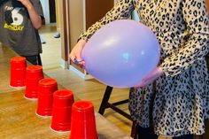 a woman is holding a balloon in front of some orange cones on the floor while another boy stands behind her