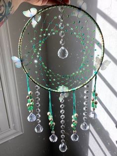 a person holding up a dream catcher made with beads and glass drops on the side